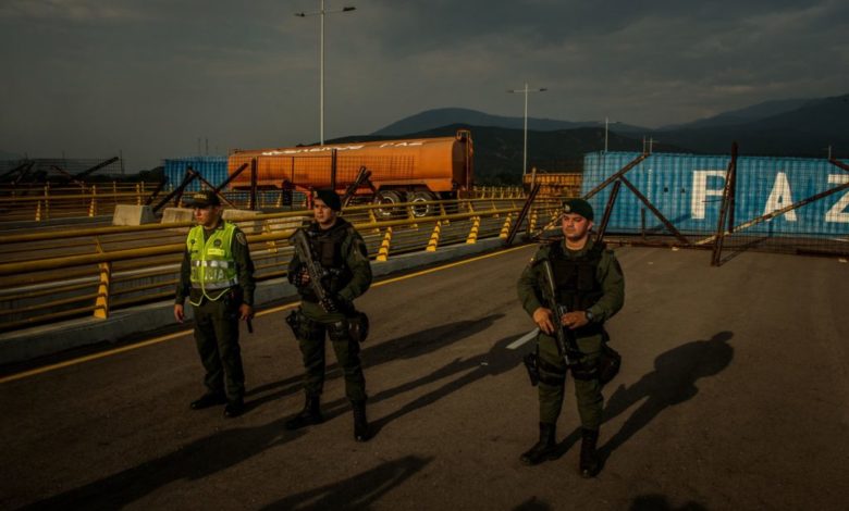 Colombian security forces stand guard in front of shipping containers placed by Venezuelan security forces to block the border bridge that connects Colombia to Venezuela.CreditCreditMeridith Kohut for The New York Times