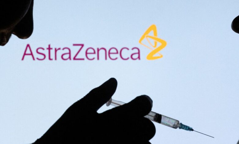 People pose with syringe with needle in front of displayed AstraZeneca logo