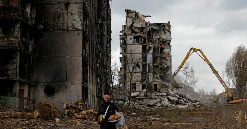 A woman reacts as she walks through her neighbourhood past destroyed apartment blocks in Mariupol