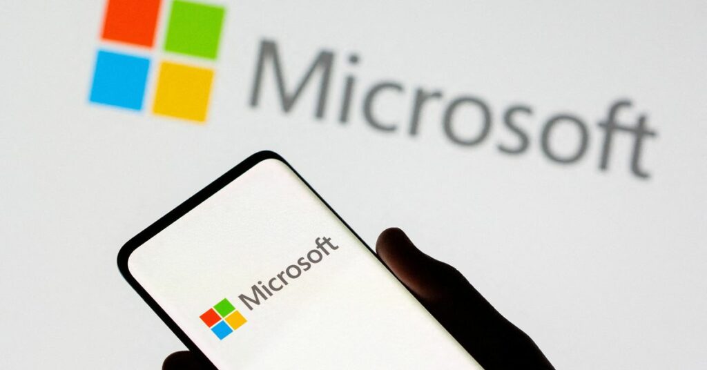 Smartphone is seen in front of Microsoft logo displayed in this illustration taken
