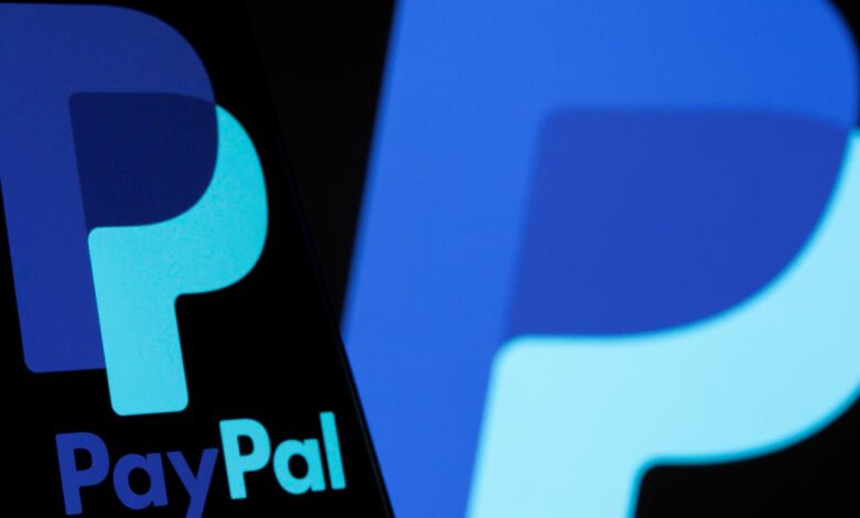 The PayPal logo is seen on a smartphone in front of the same logo displayed in this illustration
