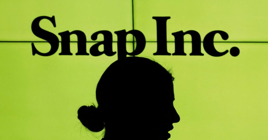 A woman stands in front of the logo of Snap Inc. on the floor of the New York Stock Exchange (NYSE) while waiting for Snap Inc. to post their IPO, in New York City
