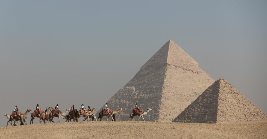 Tourists ride camels in front of the Great Pyramids plateau in Giza