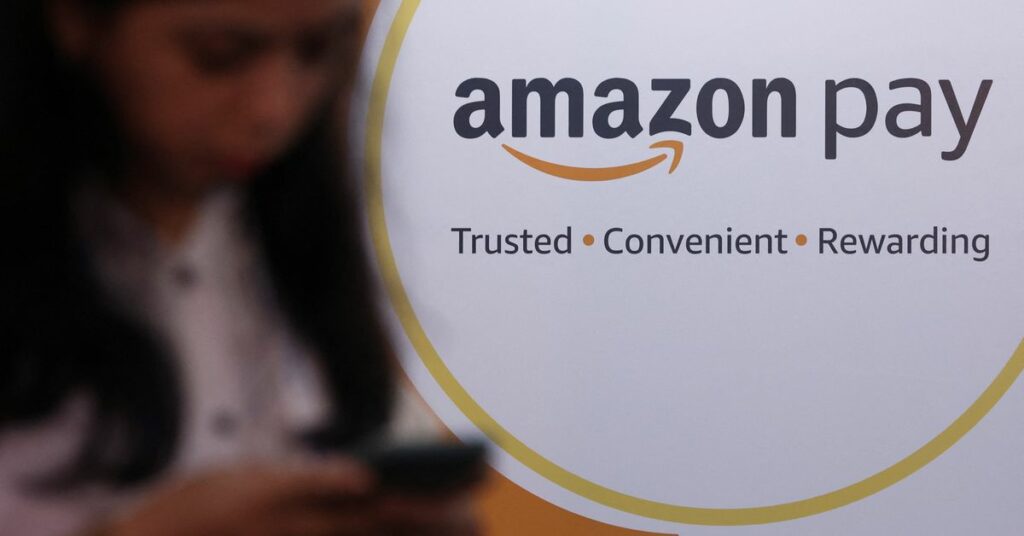 A woman uses her phone next to a logo of the Amazon Pay logo during Global Fintech Fest in Mumbai