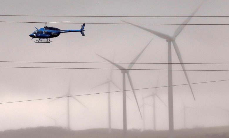 A helicopter flies near wind turbines and power lines in a paddock near the Hornsdale Power Reserve in Australia
