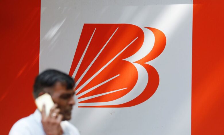 A man talks on mobile phone in front of the Bank of Baroda logo in New Delhi