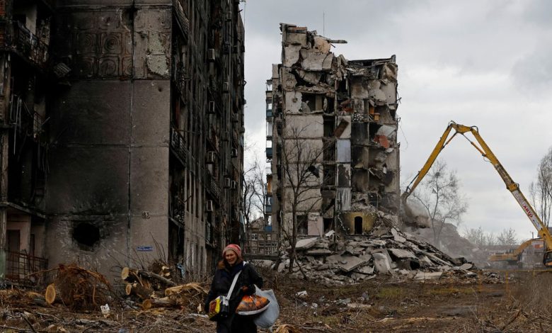 A woman reacts as she walks through her neighbourhood past destroyed apartment blocks in Mariupol