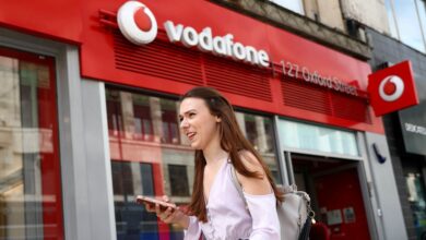 A woman holds a phone as she passes a Vodafone store in London